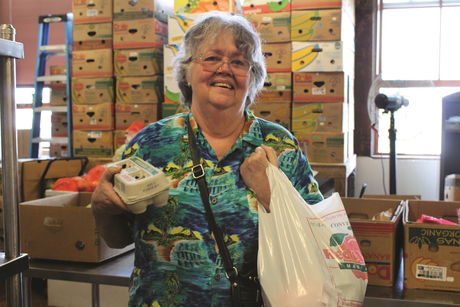 Smiling woman looks into the camera holding eggs and groceries from the food bank.