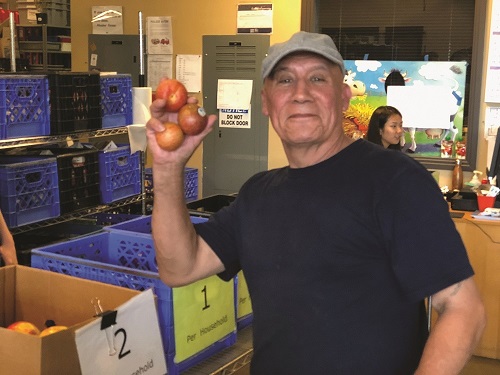 Smiling man holding up apples as he volunteers at a food bank